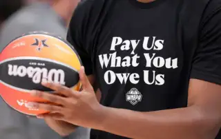 WNBA basketball player wearing t-shirt that says "pay us what you owe us"